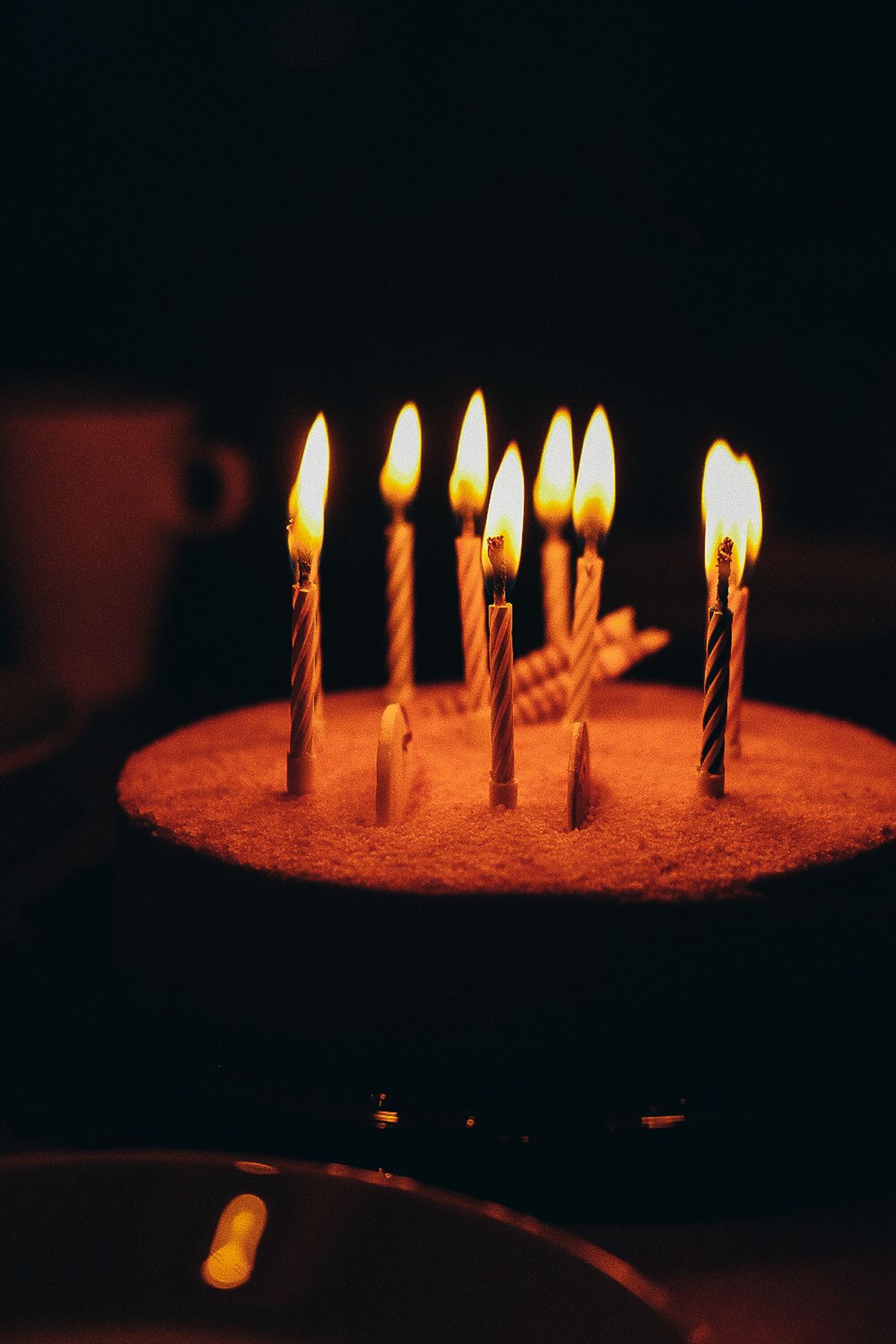 Illustrative birthday cake with glowing candles against a dark background.