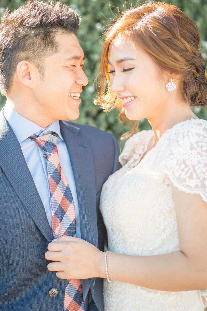 A couple smiling together outdoors, with the bride wearing lace and an updo.